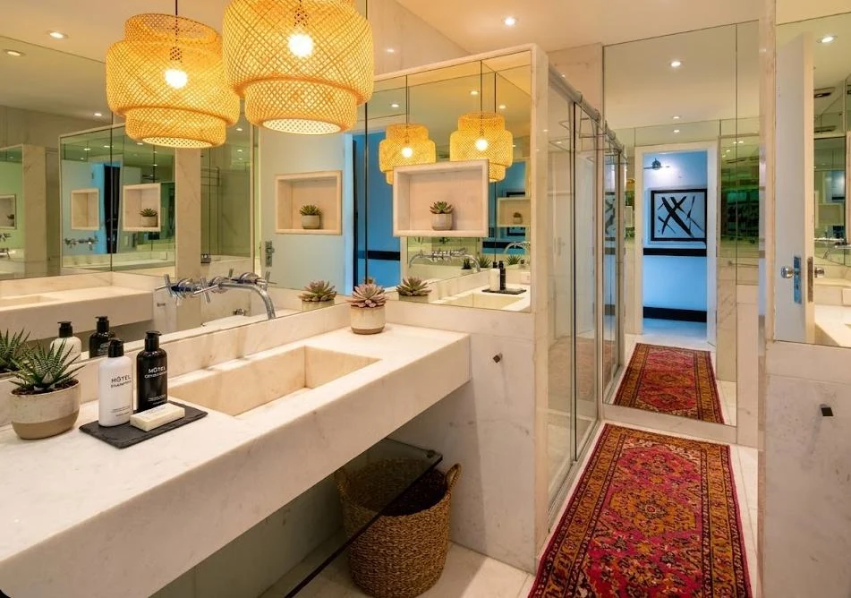 Copacabana penthouse marble bathroom after Cavmir styling — woven rattan pendants, succulents, hotel amenities, Persian runner